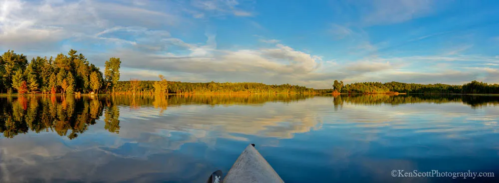 Calm, clear water of Pearl Lake at golden hour with autumn color along the far shore